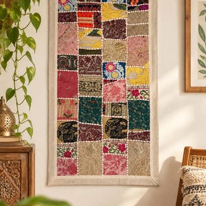 May include: A rectangular wall hanging featuring a patchwork design of various fabric squares in colours including pink, blue, green, yellow, and gold. The fabric squares are stitched together with white thread and feature floral and elephant motifs.