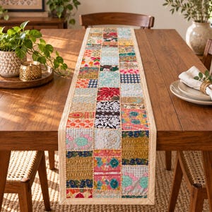 Puede incluir: Un camino de mesa rectangular con un diseño de parches de varios cuadrados de tela en colores vibrantes como rojo, azul, dorado y rosa. El camino presenta bordados intrincados, patrones florales y detalles en hilo metálico, con un borde beige sólido.