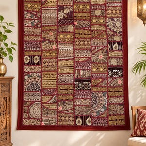 May include: A rectangular wall hanging featuring a patchwork design of various fabric panels in shades of deep red, gold, and black. The textile is decorated with intricate metallic embroidery, floral motifs, and geometric patterns throughout.