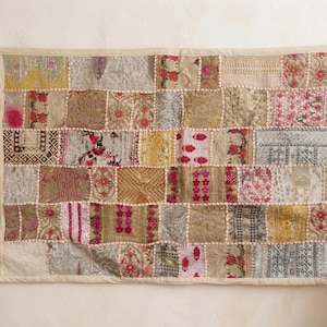 Puede incluir: Un tapiz rectangular con un diseño de patchwork de varios cuadrados de tela. El tejido muestra una mezcla de tonos dorados, beige y crema con patrones florales bordados, hilos metálicos y costuras intrincadas en tonos rosa y rojo.