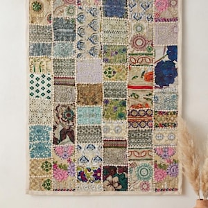 May include: A rectangular wall hanging featuring a patchwork design composed of numerous small, square fabric panels. Each panel displays a unique combination of floral, geometric, and abstract patterns in various colours, including pink, blue, green, and gold, with visible stitching and decorative borders.