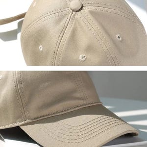 May include: Close-up of a tan baseball cap. The cap features a curved brim and a button on top. The stitching is visible, and there are small ventilation holes. The fabric appears to be a sturdy cotton or similar material.