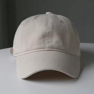 May include: A beige baseball cap with a curved brim. The cap has a six-panel design with a button on top and an adjustable strap at the back. The fabric appears to be a soft cotton or similar material.