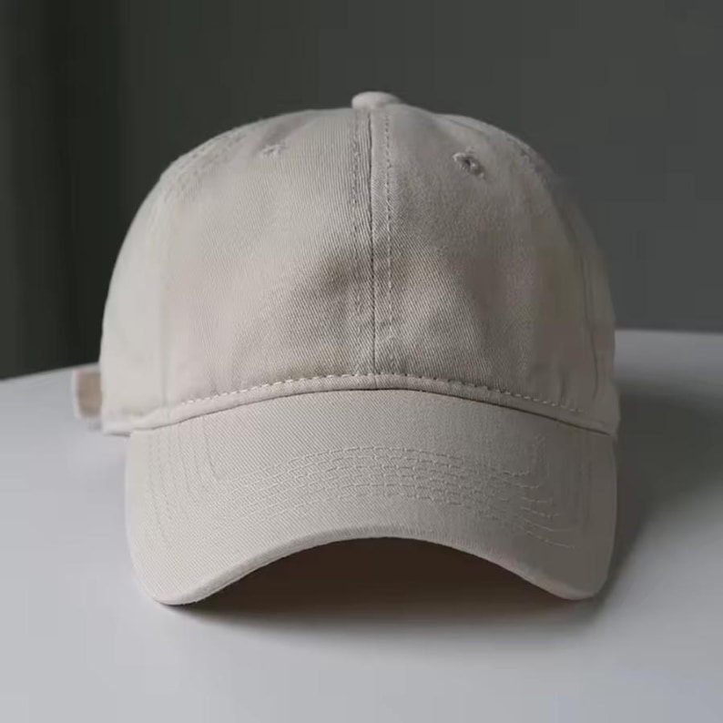 May include: A beige baseball cap with a curved brim. The cap has a six-panel design with a button on top and an adjustable strap at the back. The fabric appears to be a soft cotton or similar material.