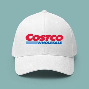 May include: White baseball cap featuring the Costco Wholesale logo in red and blue. The logo is prominently displayed on the front of the cap. The cap has a curved brim and a button on top.