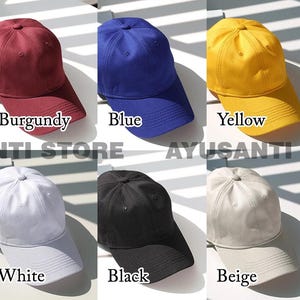 May include: A collection of baseball caps in various colors, including khaki, burgundy, blue, yellow, red, navy, white, black, beige, and grey. Each cap has a curved brim and a fabric crown. The text "AYUSANTI STORE" is visible.