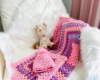 Set composto da copertina e cappellino per neonata, realizzati a mano all'uncinetto, con bordo a conchiglia testurizzato nei colori rosa, viola e pesca. Un regalo di lusso e prezioso per la cameretta.