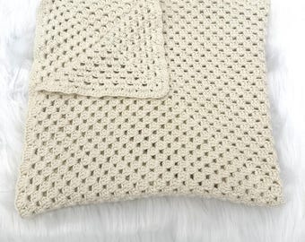 Può includere: Una federa quadrata all'uncinetto color crema caratterizzata da un classico motivo granny square con un design a punti a grappolo ripetuti. Il tessuto ha un aspetto strutturato e traforato ed è ripiegato nell'angolo superiore per rivelare l'interno.