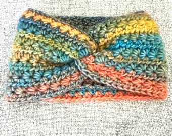 Può includere: Una fascia all'uncinetto con un design frontale intrecciato, realizzata con filato multicolore nelle tonalità del giallo, arancione, blu, verde e grigio. L'accessorio presenta un motivo a punti testurizzati a forma di stella su tutta la superficie.