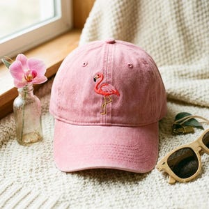 Peut inclure: Une casquette de baseball rose poudré avec un motif de flamant rose brodé sur le panneau avant. La casquette présente une visière incurvée, des œillets cousus pour la ventilation et une calotte structurée. Le flamant est en corail et noir.