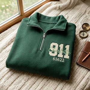 May include: A dark green quarter-zip sweatshirt featuring a silver metal zip. The front displays the large cream-coloured number 911, the name Charlotte in cursive green script, and the number 61622 printed in a smaller cream-coloured font.