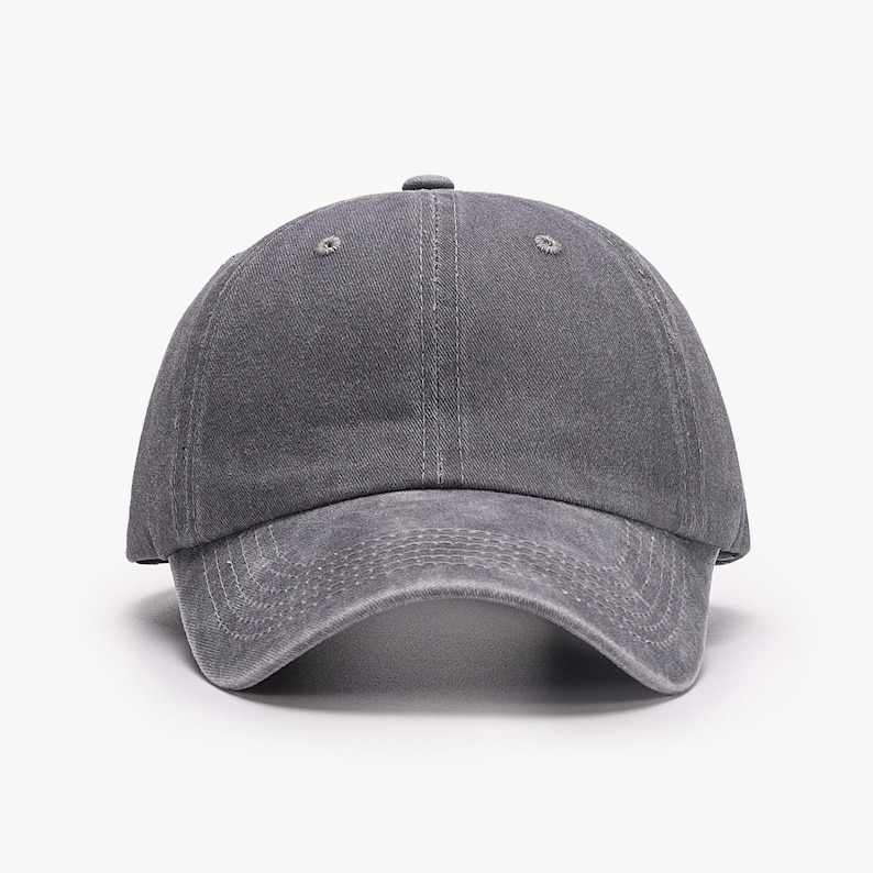 May include: A solid charcoal gray baseball cap with a distressed, washed-out fabric texture. The cap features a six-panel construction with a curved brim, stitched eyelets on the crown, and visible tonal stitching along the front visor panels.