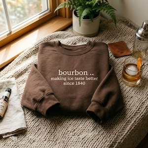 以下が含まれることがあります： bourbon .. making ice taste better since 1840という白い文字がプリントされたダークブラウンのクルーネックトレーナー。長袖で、襟、袖口、裾はリブ編みになっており、シンプルで清潔感のあるストレートなデザインの衣類です。