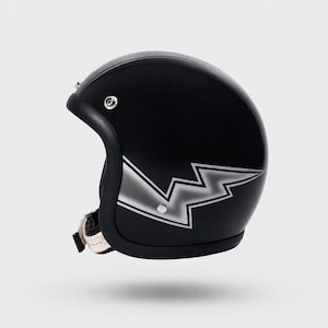 May include: A matte black open-face motorcycle helmet featuring a silver lightning bolt graphic on the side. The helmet includes a black trim along the opening, a silver metal snap button near the temple, and a chin strap with a metal buckle.