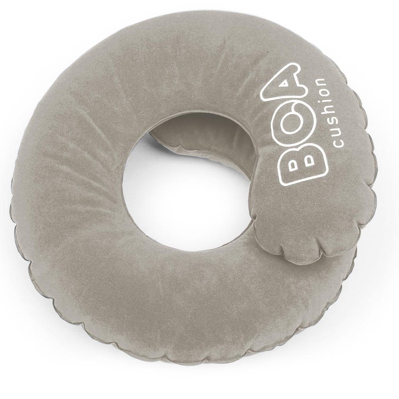 May include: A gray, inflatable travel pillow with a circular design and a central opening. The pillow has the text "BOA cushion" printed in white on the side. The pillow is designed for neck support.