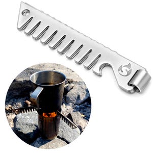 Op de afbeelding: Een roestvrijstalen campingtool met een kamachtige rand, flesopener en lus. De tool ondersteunt een metalen beker boven een klein vuur. De beker bevat een donkere vloeistof, mogelijk koffie of thee.