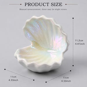 以下が含まれることがあります： 光沢のある仕上げの虹色の貝殻型ディッシュ。PRODUCT SIZEおよびManual measurement, there may be slight errorsというテキストが表示されています。寸法は高さ11.2cm、幅と奥行きは11cmです。