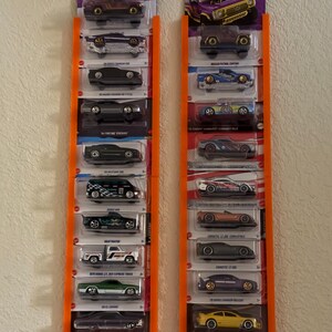 May include: Two orange display racks holding multiple Hot Wheels toy cars. The cars are in their original packaging, with various colors and designs. The packaging is purple and features the Hot Wheels logo.