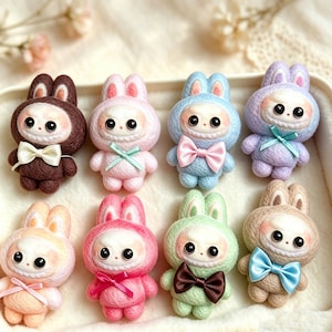 May include: Eight small, needle-felted rabbit figurines arranged in two rows. Each bunny features a textured, colored hood, large black eyes, a white face, and a satin bow. The colors include brown, pink, blue, lavender, peach, hot pink, mint, and tan.