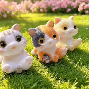 May include: Three small cat figurines with flocked textures. One is white and gray, one is calico with orange, white, and black patches, and one is light orange and white. Each cat has large dark eyes, pink noses, and sits in an upright position.
