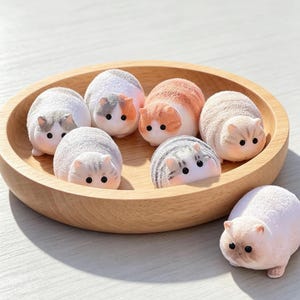 Peut inclure: Un plateau rond en bois contenant six petites figurines de chat arrondies avec divers motifs de fourrure, notamment blanc, gris, orange et marron. Chaque figurine présente de petites oreilles et des yeux noirs. Une figurine de chat assortie est posée à côté.