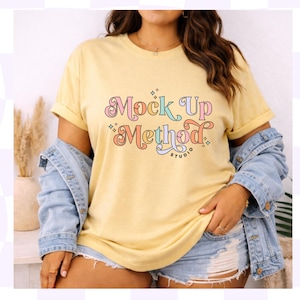 May include: A yellow t-shirt with the text "Mock Up Method" in a colorful, retro font. The shirt is worn with a denim jacket and denim shorts. The overall style is casual and relaxed.