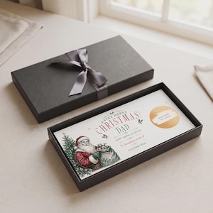 Puede incluir: Una caja de regalo rectangular negra con una cinta de satén gris, que contiene una tarjeta blanca con una ilustración vintage de Santa Claus, el texto A VERY MERRY CHRISTMAS DAD, A little surprise, just for you, Scratch to reveal, Love from Oliver y un círculo dorado para rascar con la etiqueta A ROUND OF GOLF.