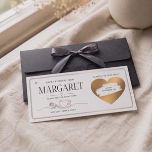 Puede incluir: Una tarjeta rectangular blanca para rascar con detalles en lámina dorada, que presenta el texto HAPPY BIRTHDAY, MUM MARGARET, THANK YOU FOR EVERYTHING y WITH LOVE, EMMA & JACK X, junto a un corazón dorado y un sobre negro con cinta gris.