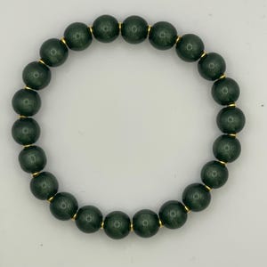 May include: A circular stretch bracelet composed of dark forest green spherical beads with a subtle shimmering finish. Each bead is separated by a small, thin, polished gold-toned metal spacer, creating a uniform pattern around the entire band.