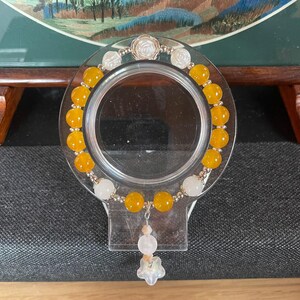 May include: A beaded bracelet featuring round yellow translucent beads, white spherical beads, and small metallic spacers. The design includes a central silver-toned rose charm at the top and a dangling charm element with a white star-shaped bead.