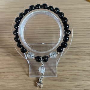 May include: A beaded bracelet featuring glossy black spherical beads with subtle gold-toned veining, interspersed with clear, textured beads. A central dangling charm shaped like a five-pointed star hangs from a silver-toned metal connector.