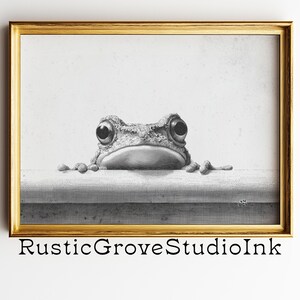May include: Black and white framed print featuring a detailed illustration of a frog with large eyes peeking over a ledge. The artwork is set in a gold-colored frame and includes the text "RusticGroveStudioInk" at the bottom.