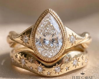 May include: A gold ring set featuring a pear-shaped center stone in a beaded bezel setting, flanked by star-shaped engravings with small inset diamonds. The matching curved band is adorned with multiple star motifs and small diamonds. Text: ELITE CARAT JEWEL.