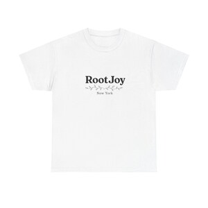 Può includere: Una t-shirt bianca a maniche corte con il testo nero RootJoy centrato sul petto. Sotto il testo si trova una piccola grafica decorativa di un sottile viticcio con foglie, seguita dalla parola New York in un semplice carattere nero.