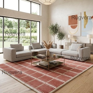 May include: A rectangular area rug featuring a terracotta red base with a white grid pattern and small vertical white dashes along the lines. The rug is positioned on a light wood floor in a living room with light gray modular sofas and a glass coffee table.