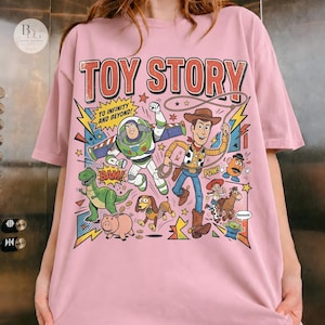 May include: Pink t-shirt featuring a colorful graphic of Toy Story characters, including Buzz Lightyear and Woody. The design includes the text "TOY STORY" and "TO INFINITY AND BEYOND!" in a comic book style.