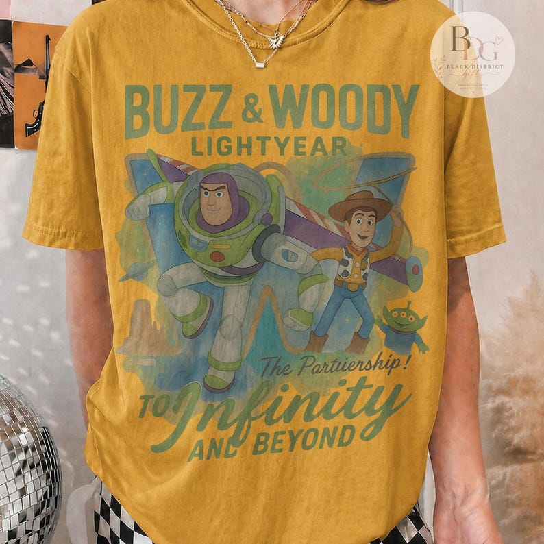 May include: Mustard yellow t-shirt featuring Buzz Lightyear and Woody from Toy Story. The graphic includes the text "BUZZ & WOODY LIGHTYEAR" and "TO INFINITY AND BEYOND". The design also includes the text "The Partiership!"