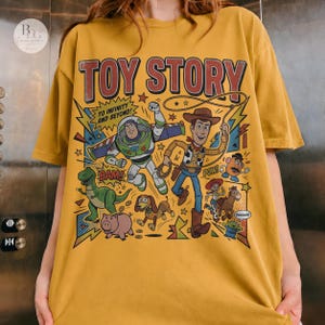 May include: Mustard yellow t-shirt featuring a colorful graphic of Toy Story characters, including Buzz Lightyear and Woody. The text "TOY STORY" is at the top, with "TO INFINITY AND BEYOND!" below. Comic book style design with stars and action words.