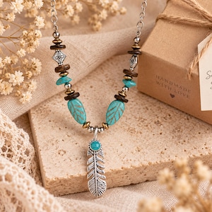 May include: A necklace featuring a silver-toned metal feather pendant with a small turquoise stone, accented by turquoise leaf-shaped beads, dark brown wooden discs, and silver-toned metal spacers on a silver-toned chain.