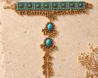 May include: A gold-toned metal hand chain featuring a wide cuff adorned with small turquoise beads in a square pattern and dangling gold spheres. A central vertical chain connects to two oval turquoise cabochons and ends in a finger loop.
