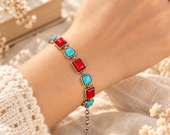 May include: A silver-toned chain bracelet featuring alternating rectangular and square settings. The settings contain smooth, vibrant red and bright turquoise stones. The bracelet includes a silver-toned metal link extension chain at the end.