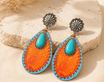 May include: A pair of drop earrings featuring a silver-toned sunburst stud connected to a large, teardrop-shaped pendant. The pendant has a bright orange center with a textured finish, bordered by a light blue scalloped edge and a central turquoise stone.