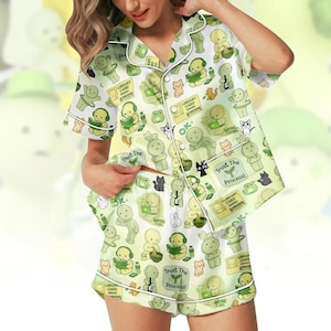 Puede incluir: Conjunto de pijama verde claro con un patr&oacute;n repetido de personajes de dibujos animados, gatos, ranas y texto. El conjunto incluye una camisa de manga corta con botones y pantalones cortos a juego, ambos con ribete blanco. El texto incluye "Trust The Process!" y "Library Card".