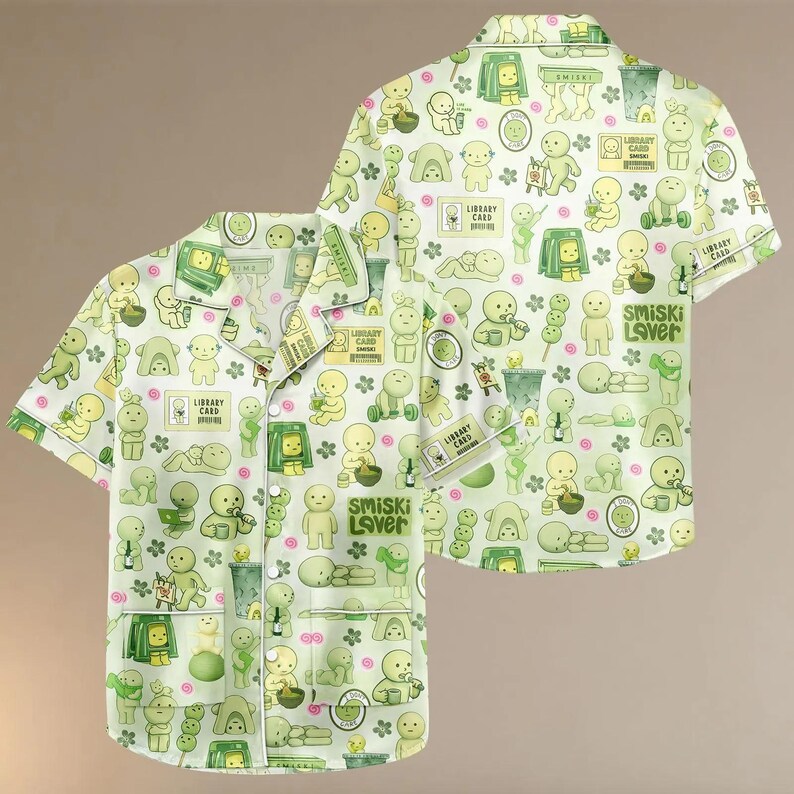 Puede incluir: Conjunto de pijama verde claro con un patr&oacute;n repetido de personajes de dibujos animados, flores y elementos tem&aacute;ticos de biblioteca. La camisa tiene mangas cortas y una parte delantera abotonada. El texto "SMISKI Lover" y "Library Card" son visibles.