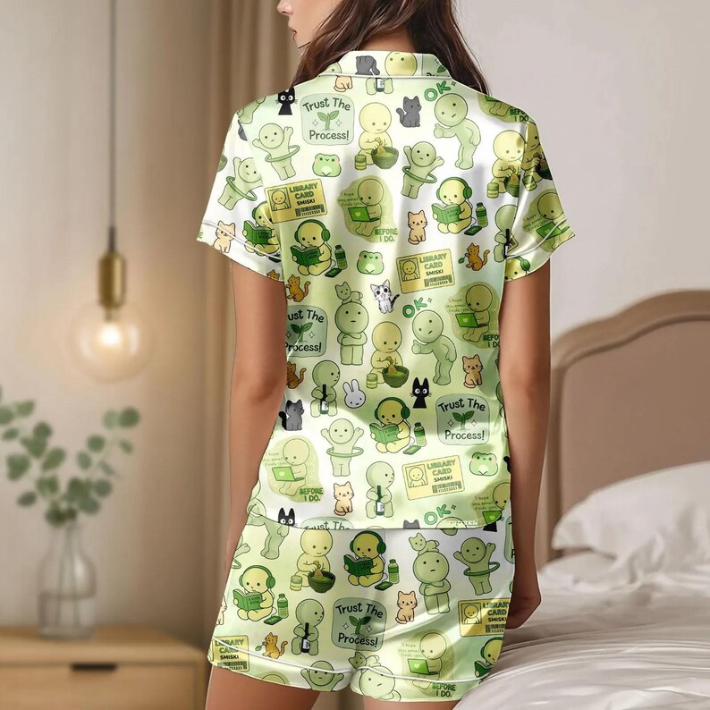 Puede incluir: Conjunto de pijama verde claro con un patr&oacute;n repetido de personajes de dibujos animados, gatos y texto. El texto incluye "Trust The Process!" y "Library Card". La camiseta de manga corta y los pantalones cortos son de material sedoso.