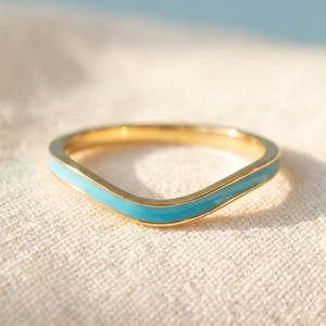 May include: A gold-toned chevron-shaped ring featuring a smooth, vibrant turquoise blue enamel inlay that follows the V-shaped contour of the band. The ring has a polished metallic finish and a consistent, thin width throughout its entire design.