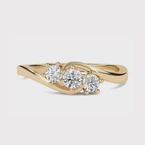 May include: A gold ring with three clear, round gemstones set in a flowing design. The band is gold-coloured, and the gemstones are evenly spaced. The ring's design is elegant and eye-catching.
