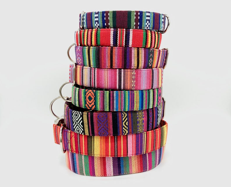 K&ouml;nnte beinhalten: Ein Stapel bunter Hundehalsb&auml;nder mit verschiedenen gestreiften und gemusterten Designs. Die Halsb&auml;nder sind aus gewebtem Stoff und haben silberne Metallverschl&uuml;sse.