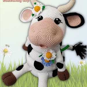 May include: A handmade crochet cow stacking toy. The white cow has black spots, brown hooves, and a pink nose. It is adorned with daisy flowers and has the word "COW" and "stacking toy" in the image.