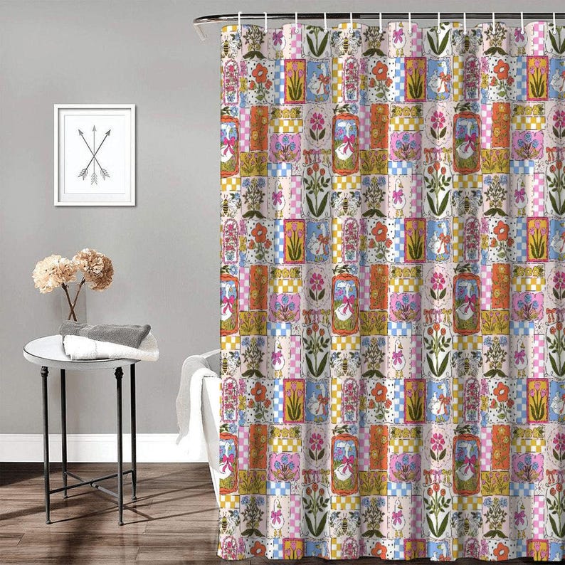 May include: A shower curtain featuring a repeating patchwork pattern of geese wearing pink bows, colorful floral arrangements, and checkered squares in shades of orange, pink, yellow, and blue, suspended from a metal rod with white curtain rings.